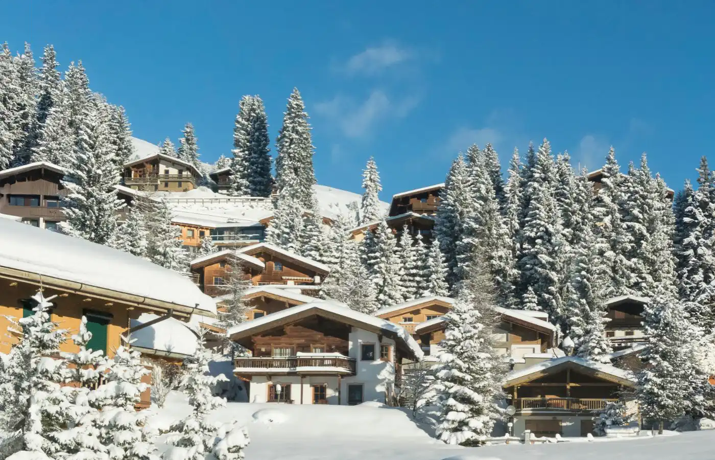 Chalets enneigés dans une station de ski alpine, entourés de sapins et de montagnes sous un ciel bleu clair.