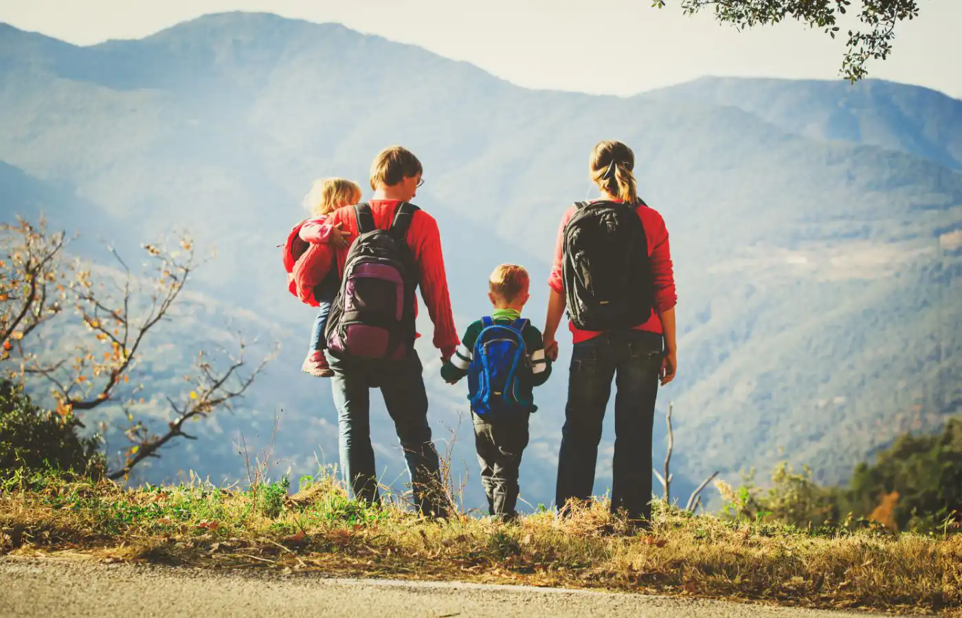 Famille en randonnée dans un paysage montagneux, parents et enfants portant des sacs à dos et admirant la vue.