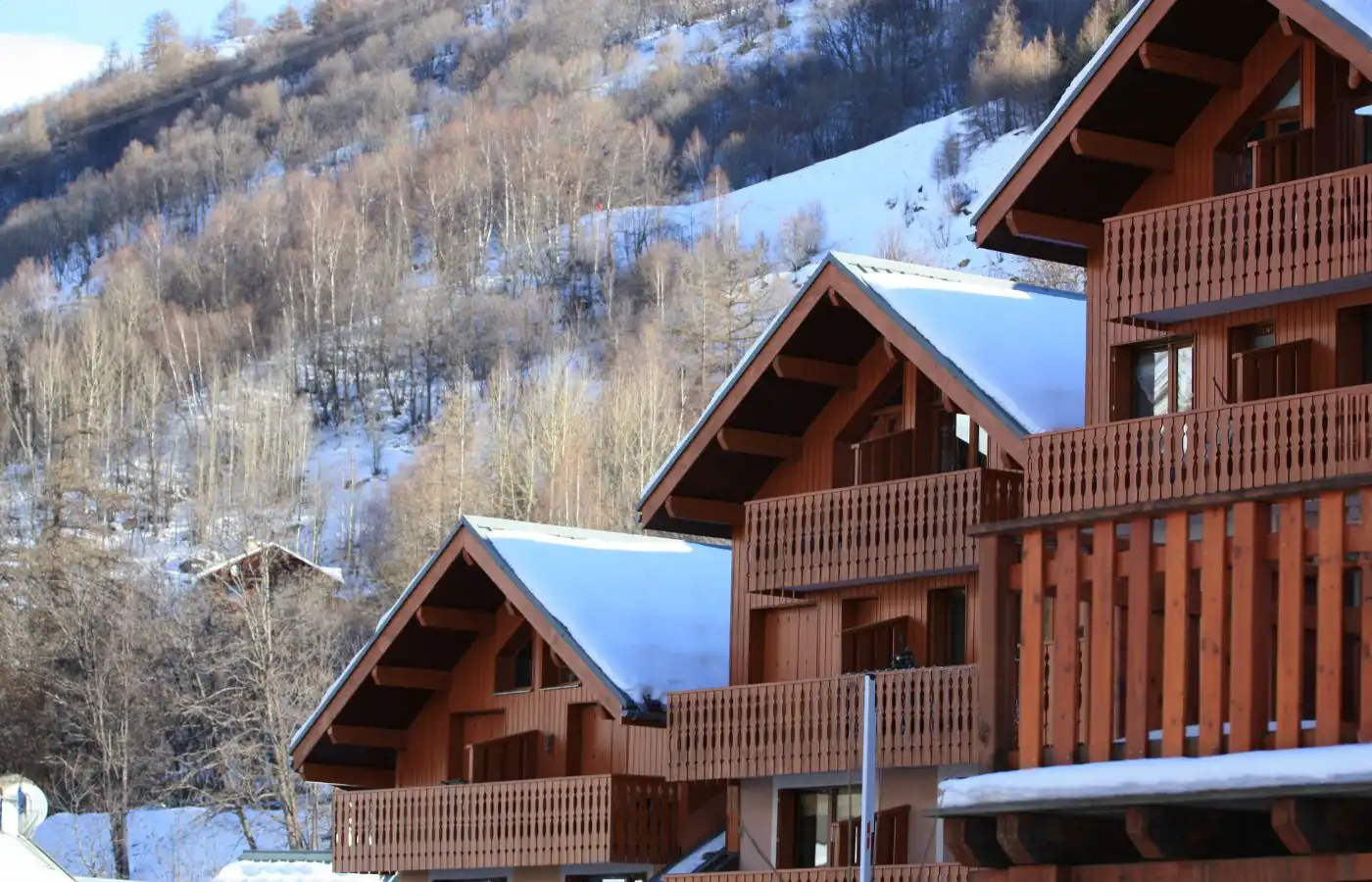 Chalets en bois dans une station de montagne enneigée, avec un cadre naturel boisé en arrière-plan.