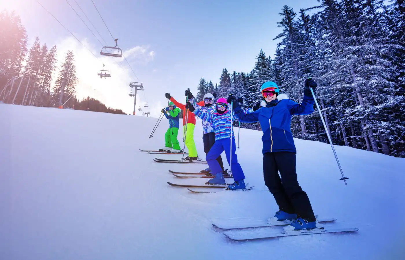 Groupe de skieurs souriants sur une piste enneigée avec des remontées mécaniques en arrière-plan, illustrant des vacances à la montagne en hiver.