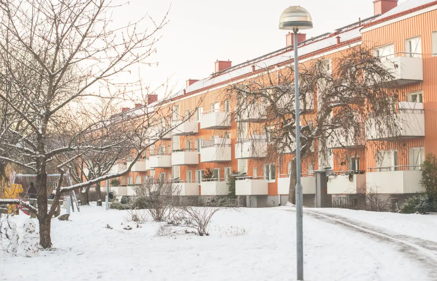 Bâtiment d'appartements résidentiels en hiver, entouré de neige, avec des arbres dénudés et un chemin enneigé.