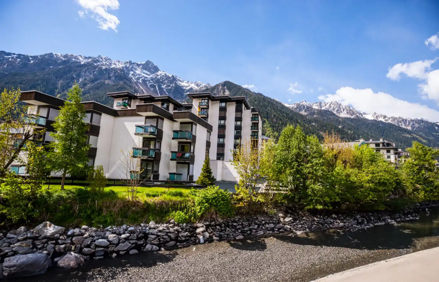 Appartements en montagne avec vue sur la nature verdoyante et les montagnes, sous un ciel bleu en été.