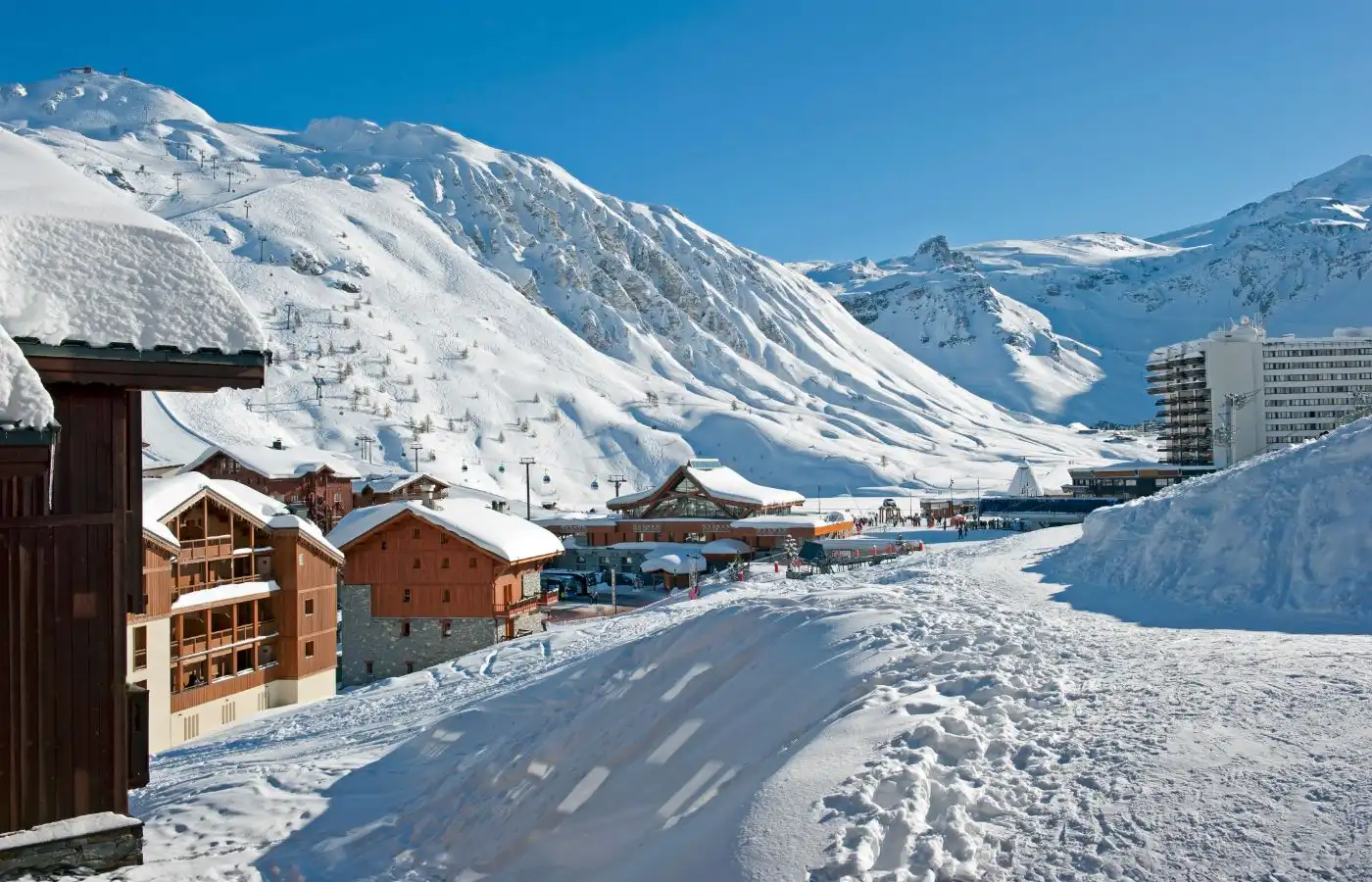 Appartements en station de ski entourés de montagnes enneigées et de pistes, sous un ciel bleu clair.