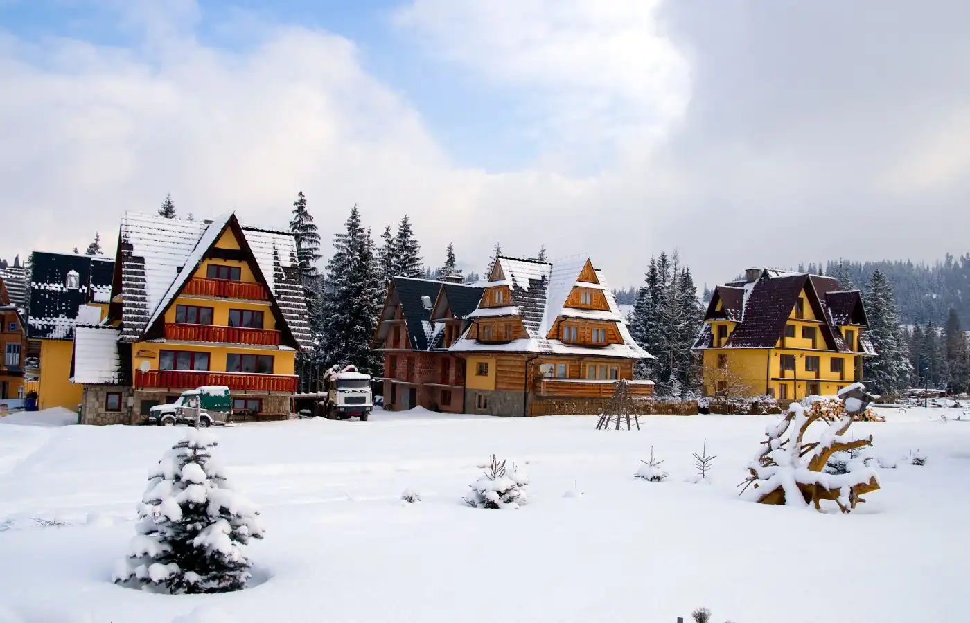 Appartements et chalets typiques dans une station de montagne enneigée, entourés de forêt et d'un paysage hivernal.